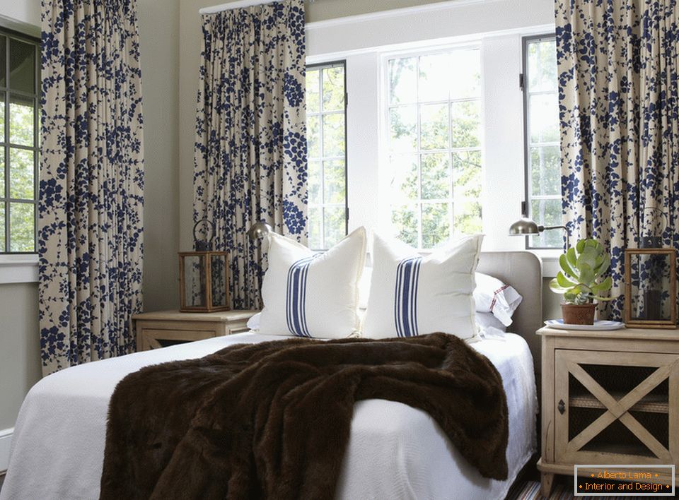 Сините цвеќиња на завесите и лентите на перниците хармонично се комбинираат во внатрешноста на спалната соба