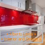 Бело мебел и црвена престилка во внатрешноста на кујната