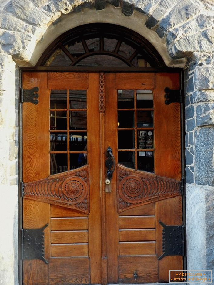 Вратите во стилот на Арт Нову ги украсуваат влезната врата на земјата куќа со фасада направена од природен камен. 