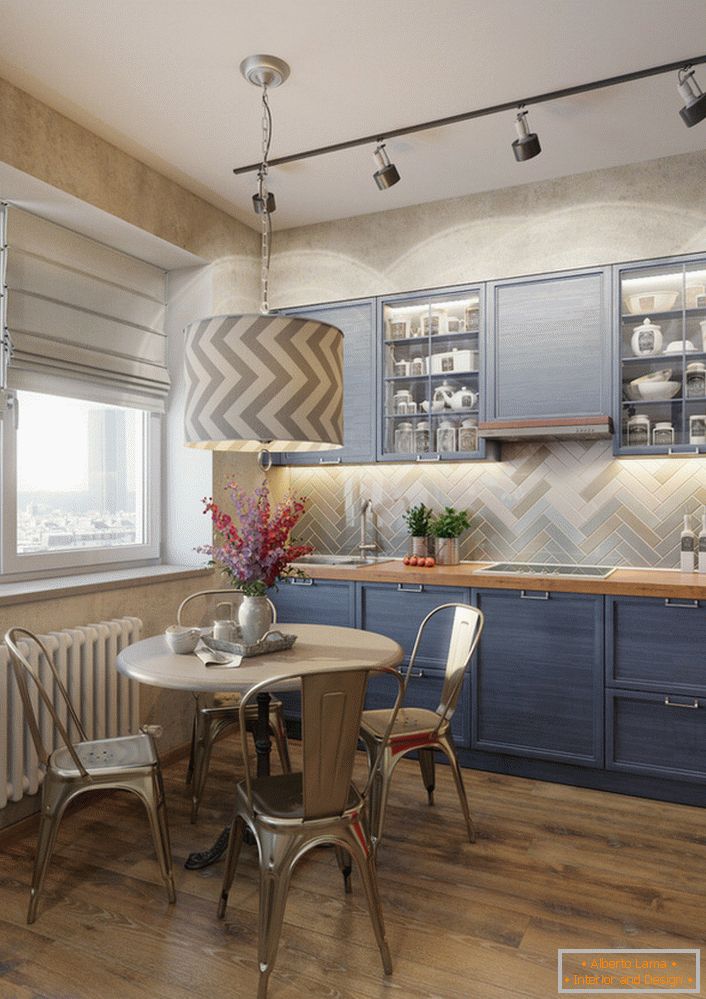 Бледата сина боја на кујнскиот сет е одлично решение за еклектична кујна. Пример за совршено избрано осветлување, кое посебно ја осветлува работната површина и трпезариската маса.